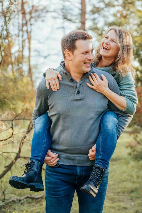 Ein lächelndes Paar, der Mann trägt die Frau auf dem Rücken, umgeben von Natur.