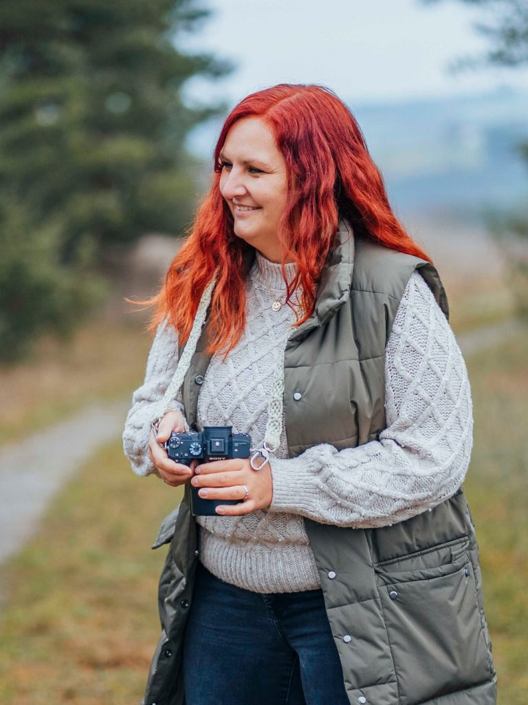 fotograf main spessart Frau mit rotem Haar, die in einem Waldgebiet mit Kamera unterwegs ist.