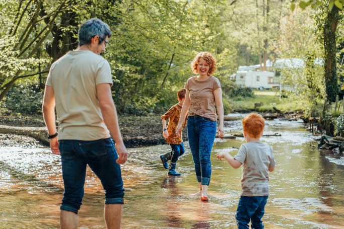 Familie beim Spielen in einem kleinen Bach in der Natur, umgeben von Bäumen.