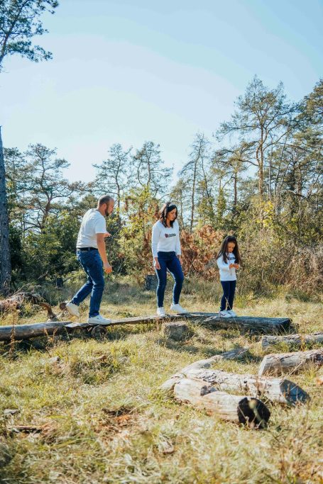 Familie wandert im Wald über Baumstämme an einem sonnigen Tag.