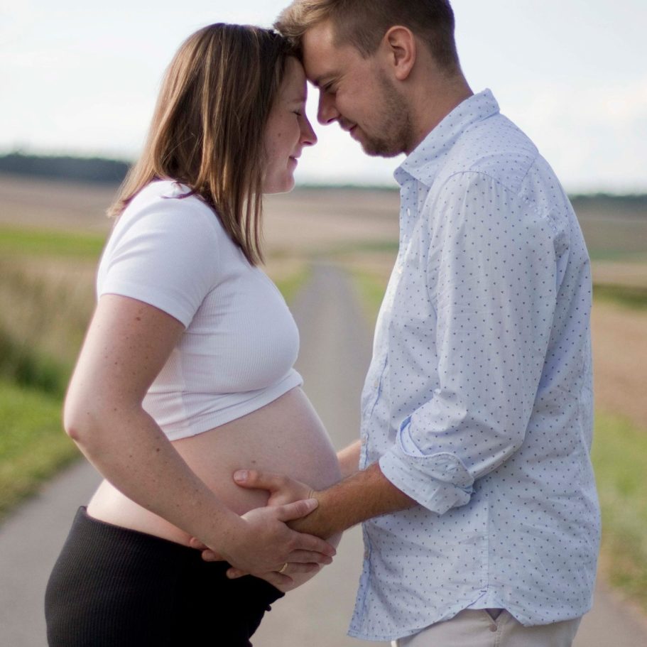 Schwangere Frau und Mann umarmen sich liebevoll auf einem Landweg.