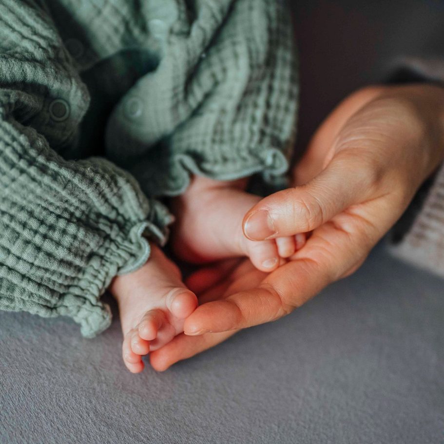 Ein Babyfuß liegt in der Hand eines Erwachsenen. Beide sind sanft und zart.