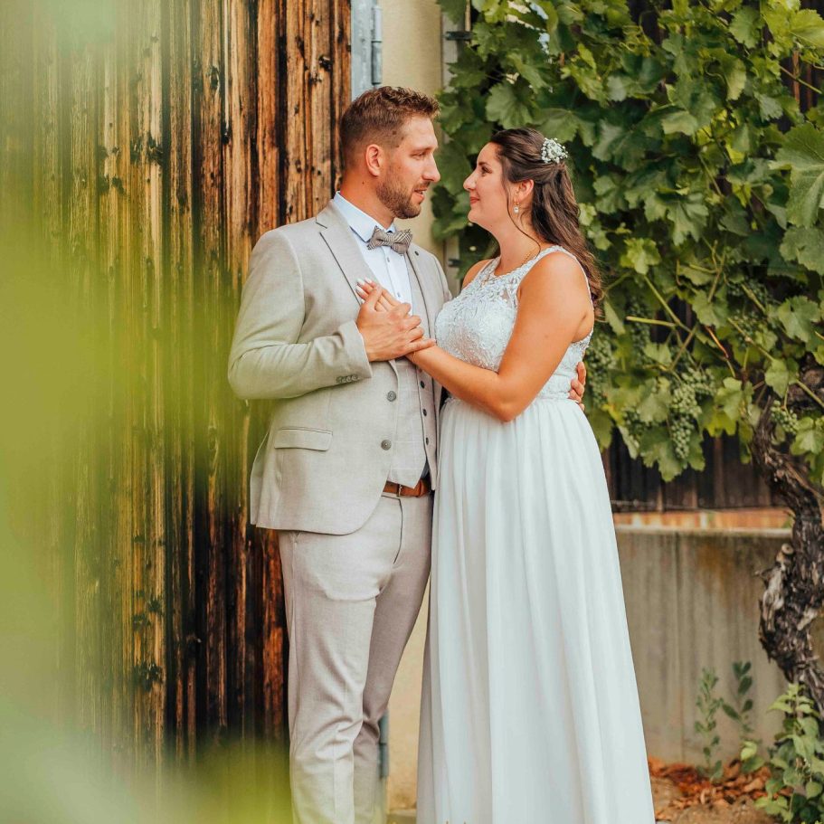 hochzeitsfotos wuerzburg Braut und Bräutigam posieren romantisch vor einer rustikalen Kulisse mit Weinreben.