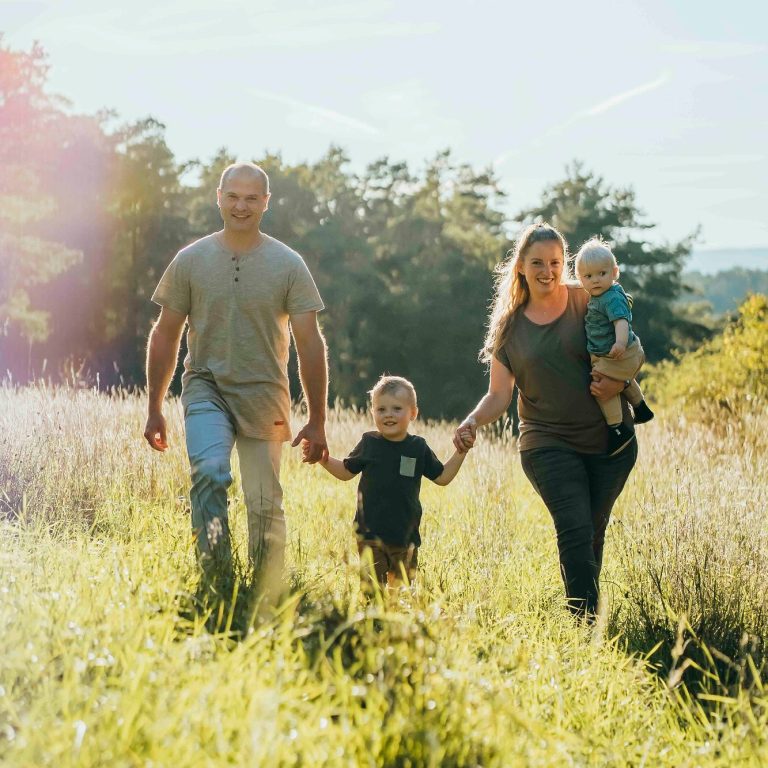 Eine Familie mit zwei Kindern geht hand in hand durch ein Feld.