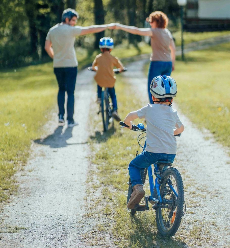Familie mit zwei Kindern auf Fahrrädern, die auf einem Weg in der Natur unterwegs sind.