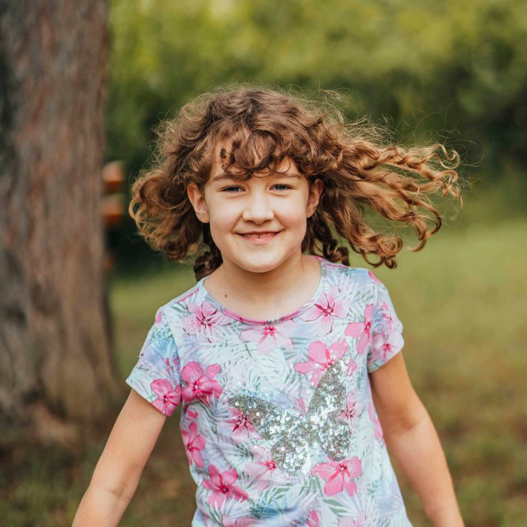 Fröhliches Mädchen mit lockigem Haar in einem bunten T-Shirt, spielt im Freien.