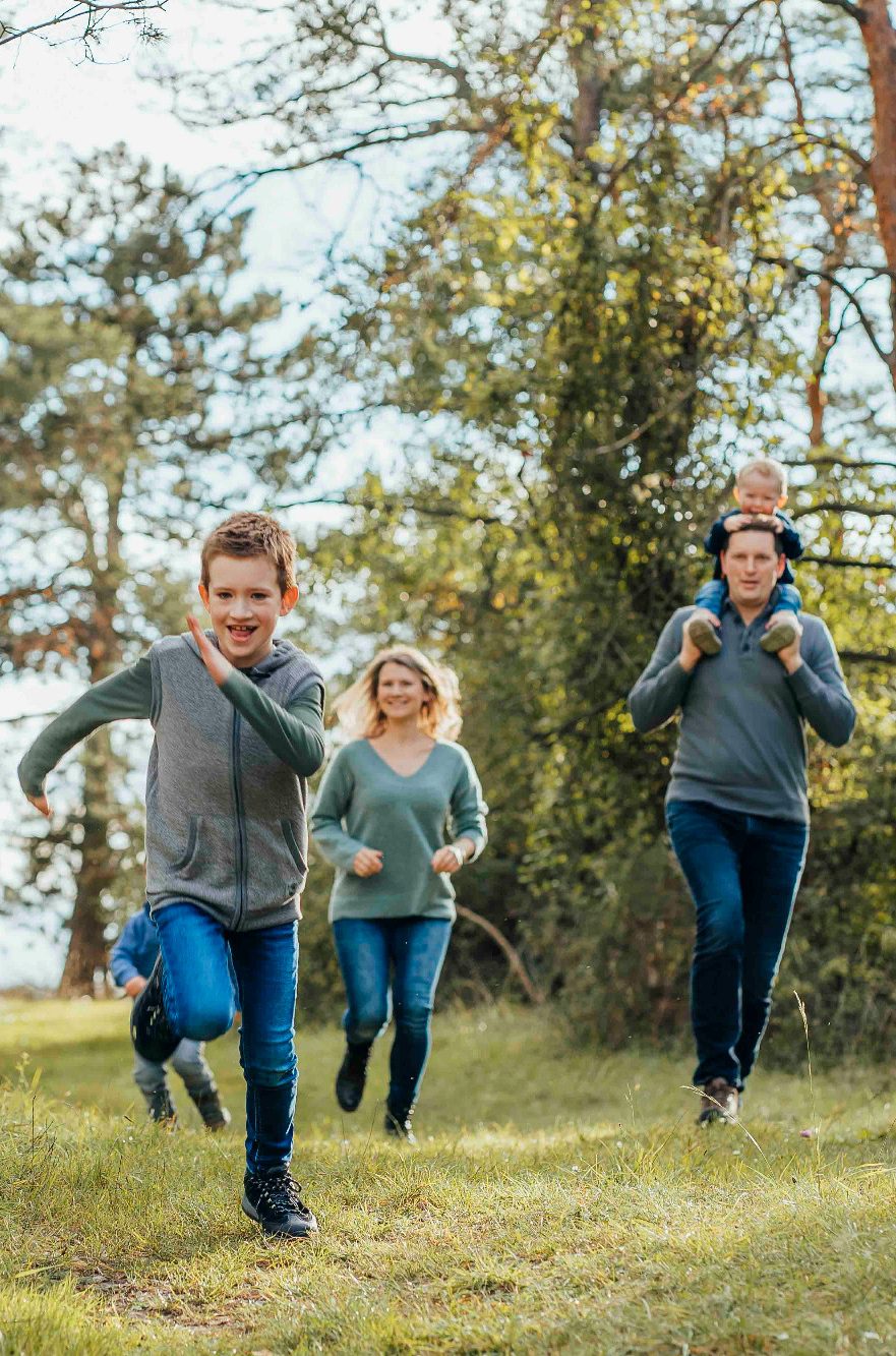 Eine Familie läuft fröhlich im Freien, Kinder spielen und die Eltern begleiten sie.