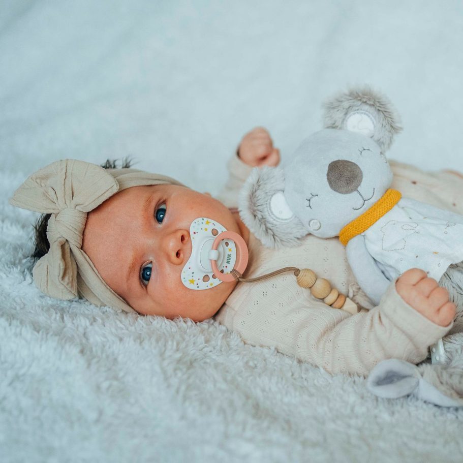 Ein Baby mit Schnuller, das ein KOALA-Kuscheltier auf einer Decke hält.