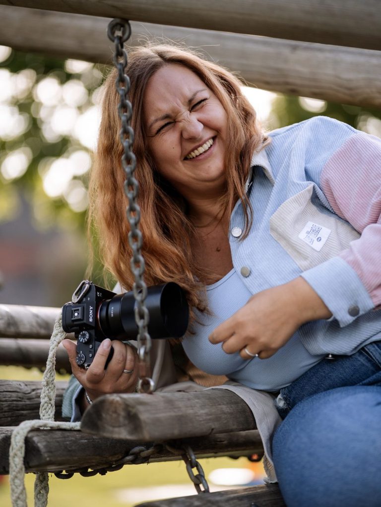 Fotografin in Main Spessart Lächelnde Frau mit Kamera sitzt auf einem Spielplatzgerät.