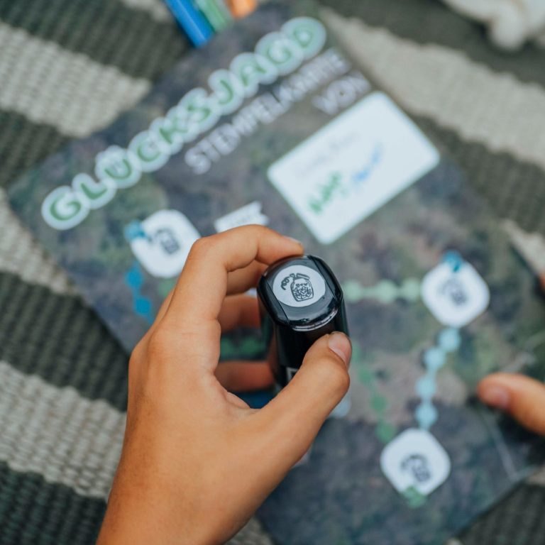 Eine Hand hält einen Stempel über einem Plan mit Wegmarkierungen für eine Schnitzeljagd.