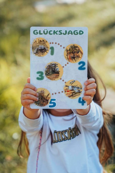 Ein Kind hält ein Spielblatt mit Zahlen und Bildern für eine Schatzsuche.