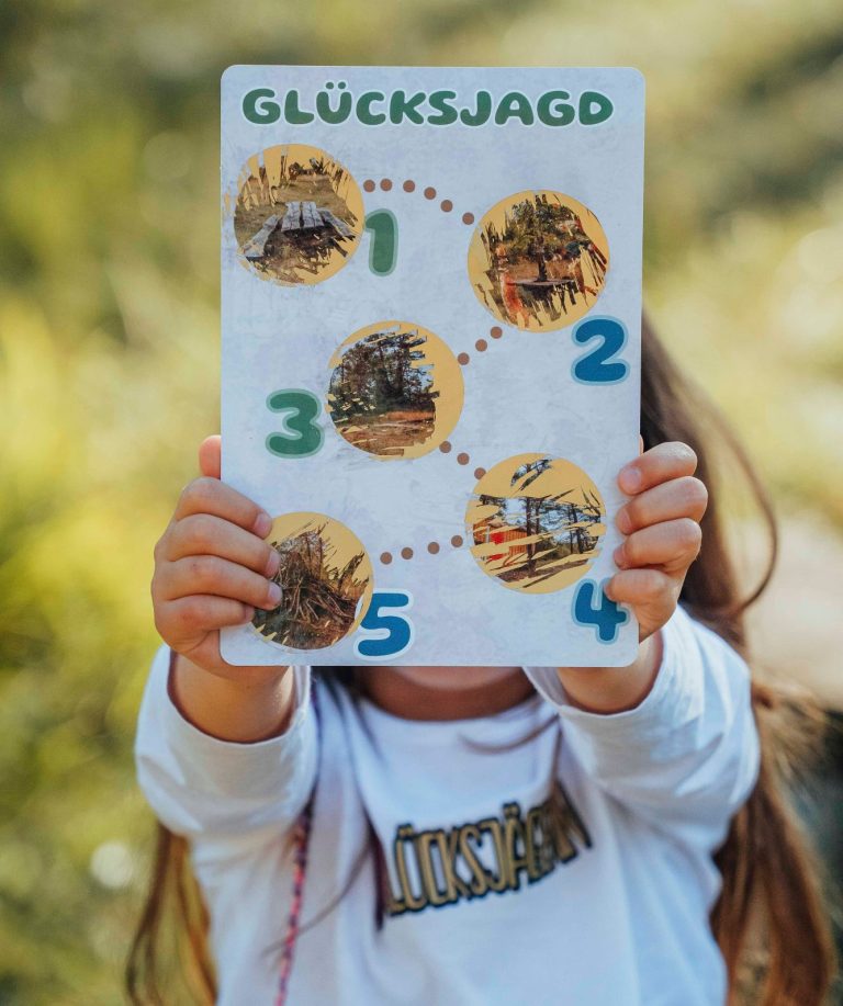 Ein Kind hält ein Spielbrett mit Zahlen und Bildern für eine Schatzsuche hoch.