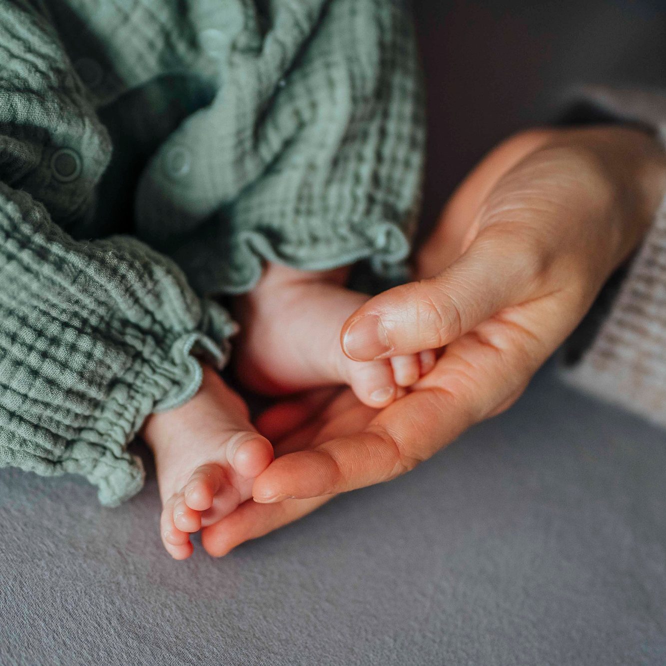 Babyfotos Main Spessart Eine Hand hält die Füße eines Babys, beide in einem sanften, grünen Stoff.