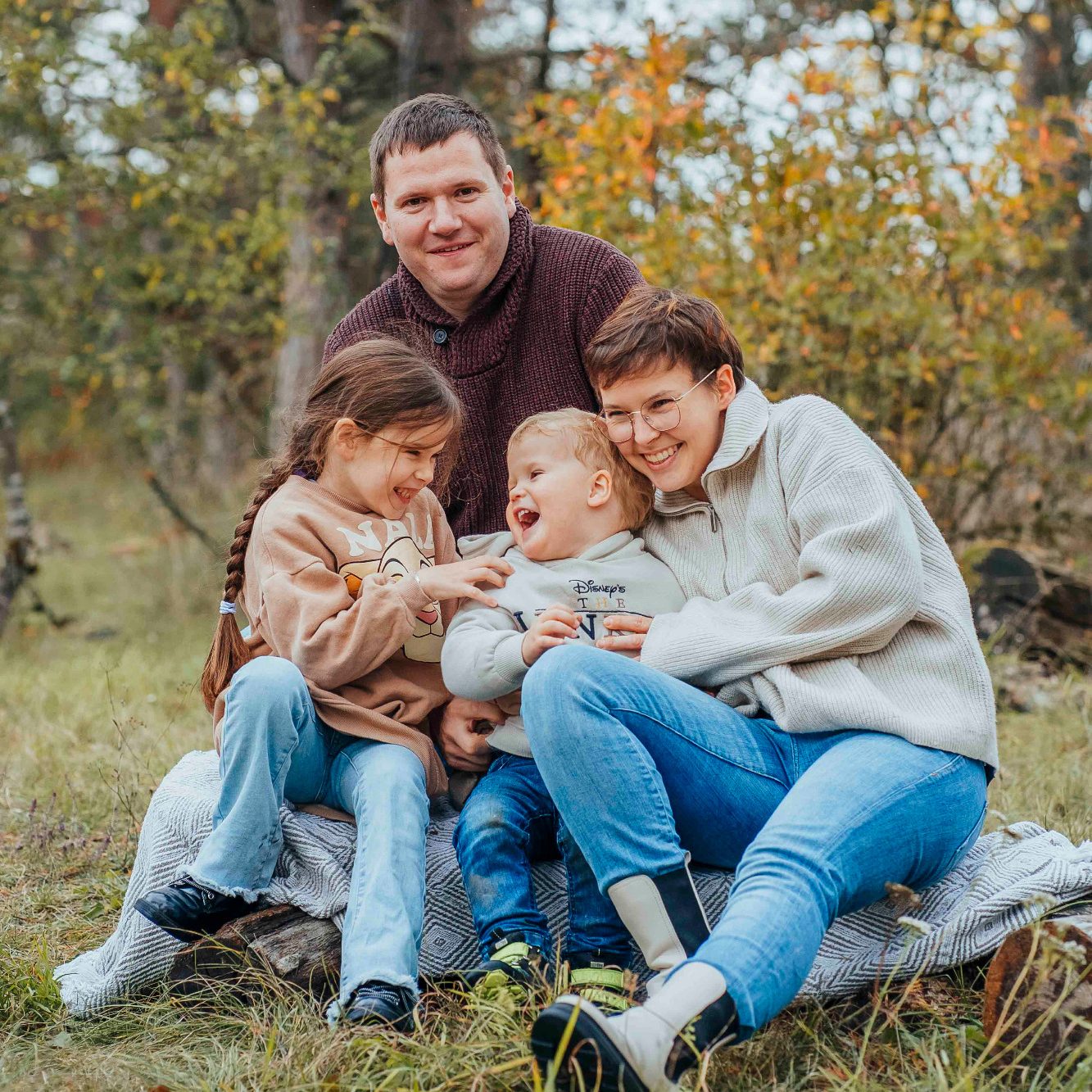 Familienfotos in Main Spessart Familie sitzt im Freien auf einer Decke, umgeben von herbstlichen Bäumen.