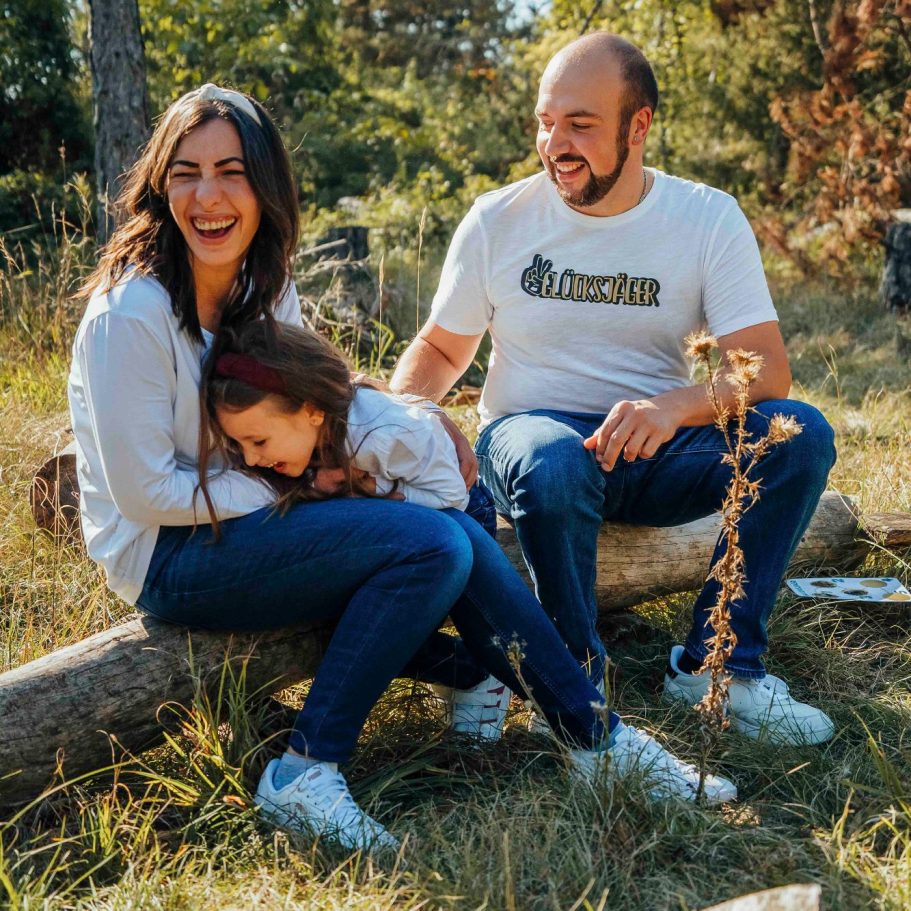 Familie sitzt im Freien auf einem Baumstamm, lächelt und hat Spaß miteinander beim Familienshooting in Marktheidenfeld.