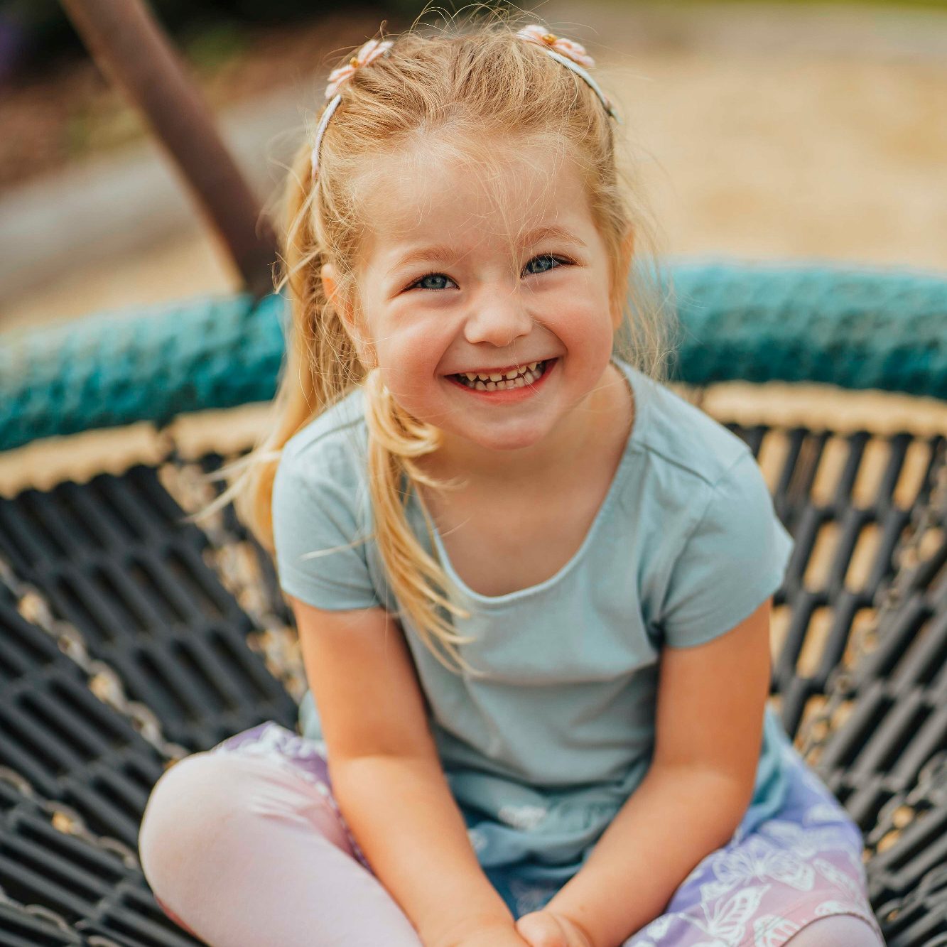 Fotograf Kindergarten Main Spessart Ein lächelndes Mädchen sitzt auf einer Schaukel und trägt ein blaues T-Shirt.