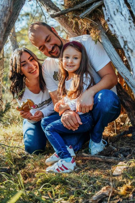 Familie posiert in der Natur, Eltern mit Tochter, lächelnd und umarmend.