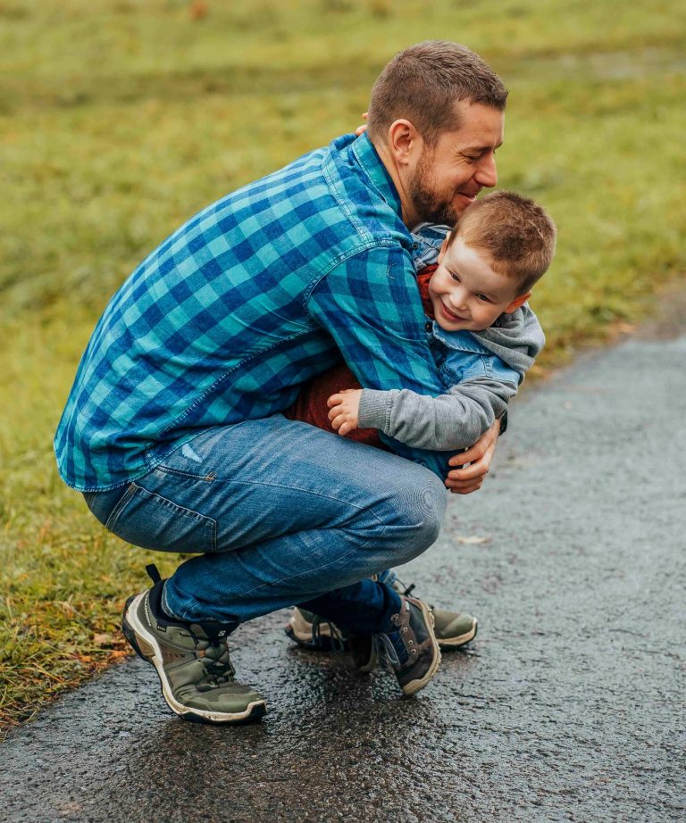 Vater umarmt lachend seinen Sohn auf einem Weg in der Natur.