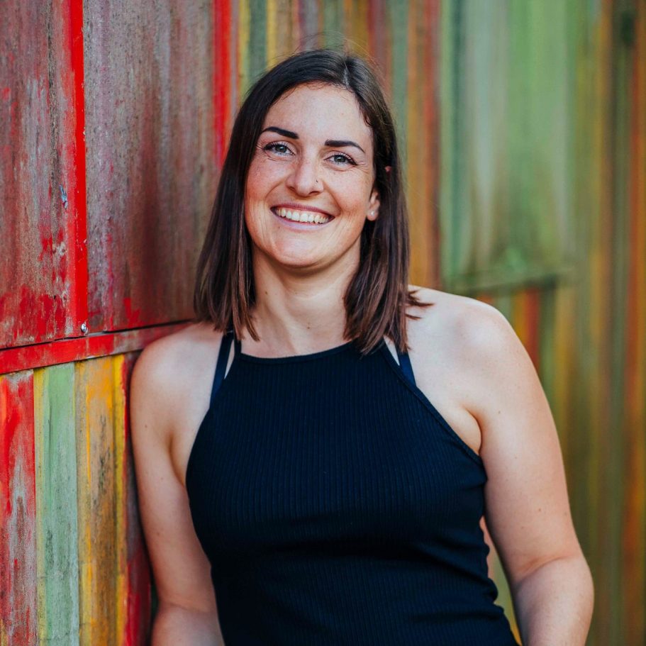 Businessportrait Wuerzburg Junge Frau lächelt vor einer farbenfrohen Wand aus Holzlatten.