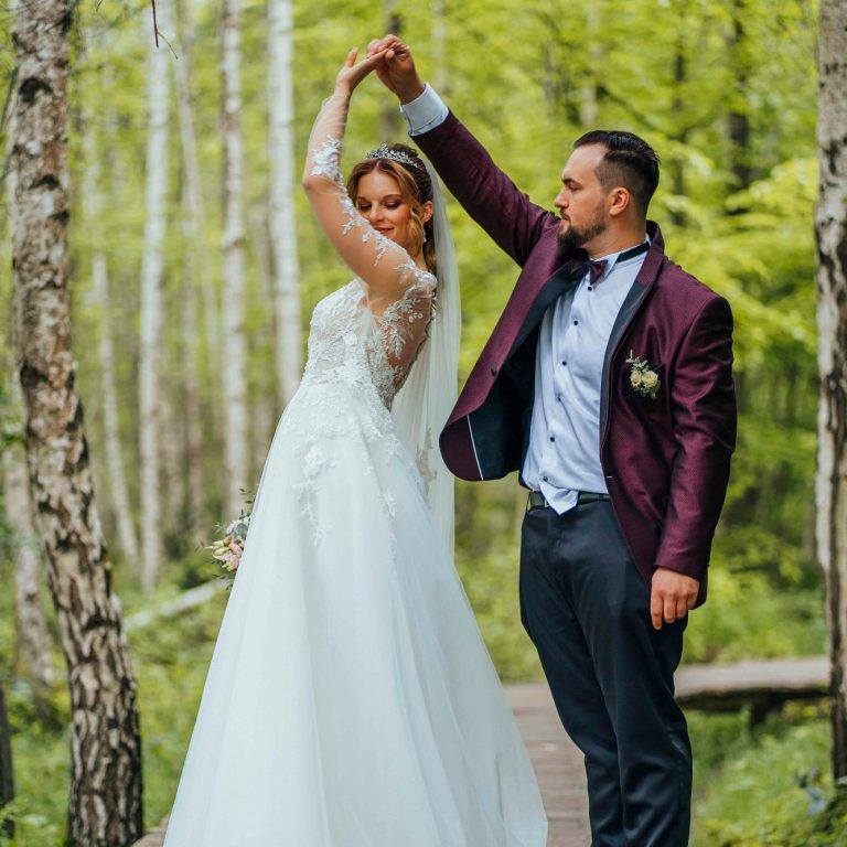 Ein Brautpaar tanzt in einem Wald, umgeben von grünen Bäumen.