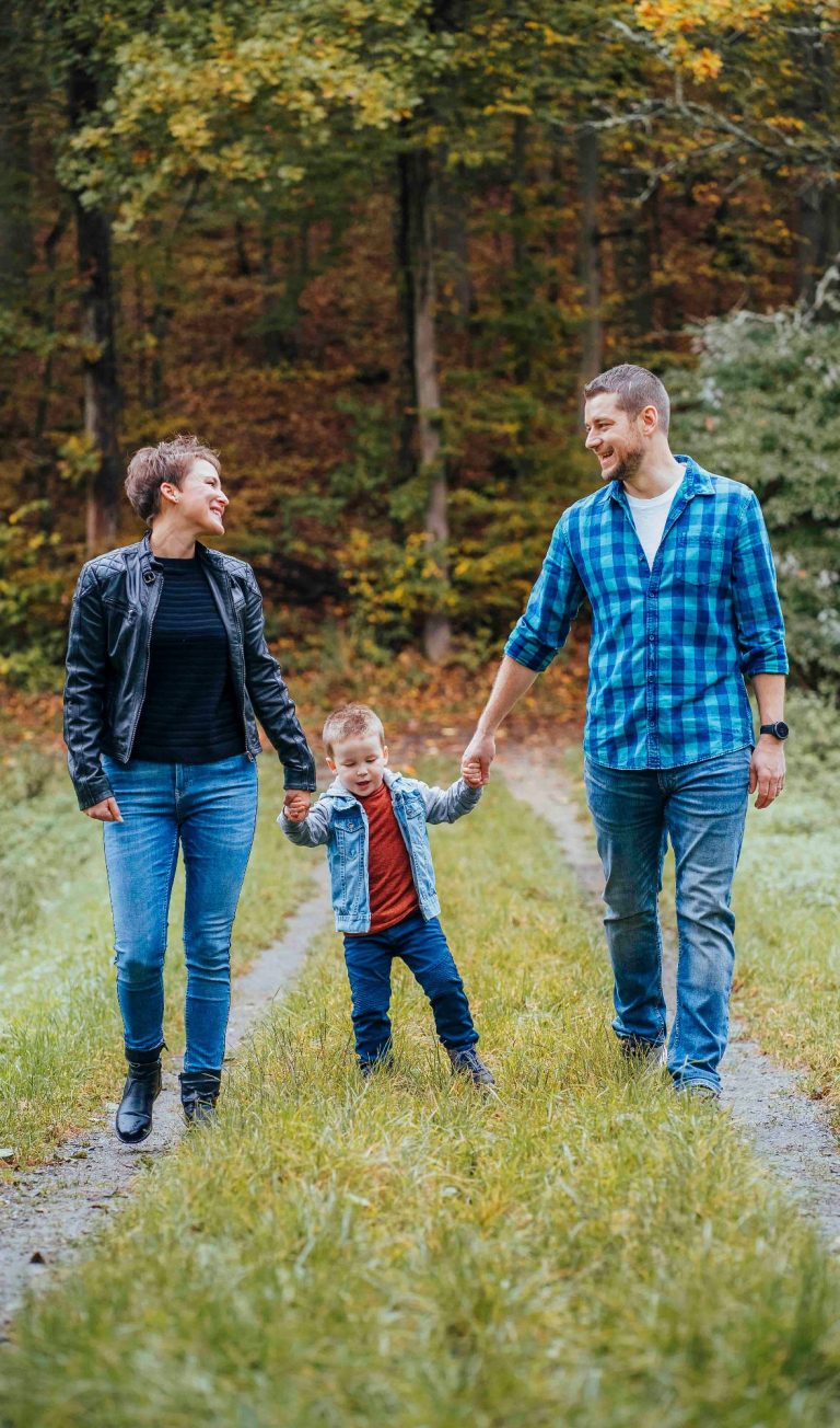 Familie beim Spaziergang im Wald, Eltern halten die Hände ihres Kindes.