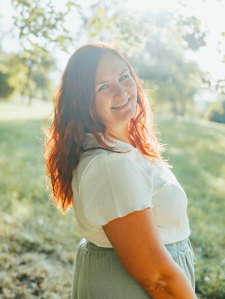 fotografin wertheim Lächelnde Frau mit rotem Haar steht im Freien vor einer grünen Wiese.