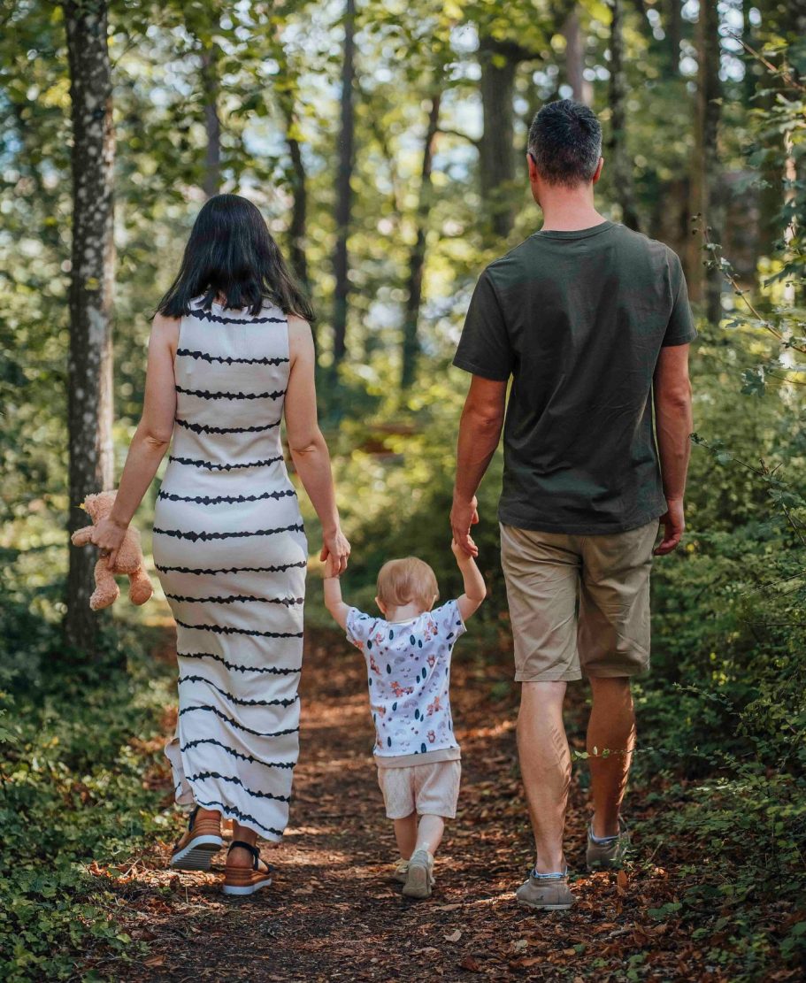 fotografin-wertheim Familie spaziert Hand in Hand einen Waldweg entlang, das Kind in der Mitte.