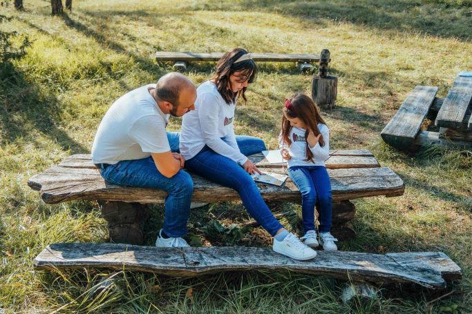 Eine Familie sitzt auf einer Bank im Freien und schaut gemeinsam auf ein Gerät.