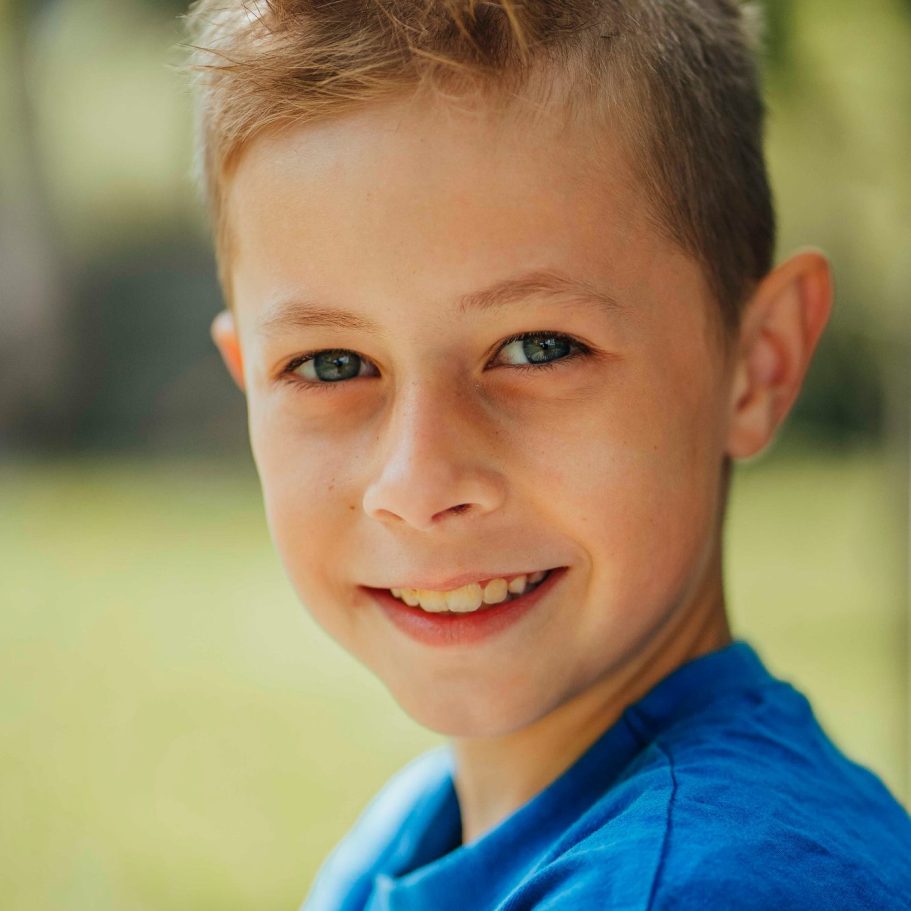 Ein lächelnder Junge mit blonden Haaren trägt ein blaues T-Shirt.