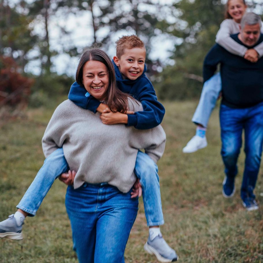 Fotograf Wertheim Familie läuft im Freien, Kinder auf den Schultern der Erwachsenen, fröhliche Stimmung.