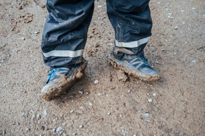Schmutzige Schuhe einer Person stehen auf einem matschigen Boden.