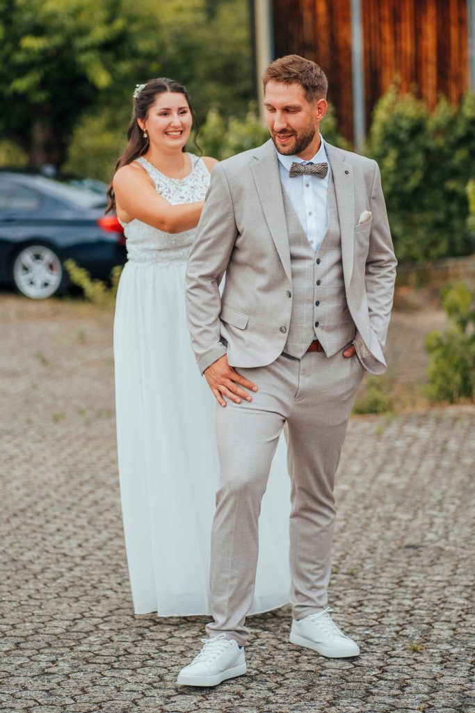 Ein Bräutigam in einem hellen Anzug steht vor einer Braut in einem weißen Kleid.