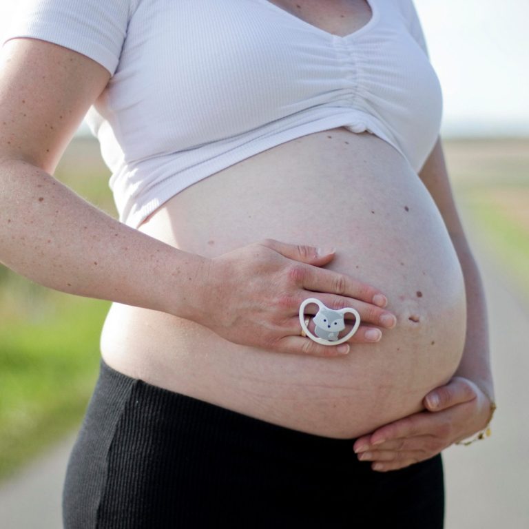 Schwangere Person mit einem Ring, die den Bauch auf einer Straße hält.