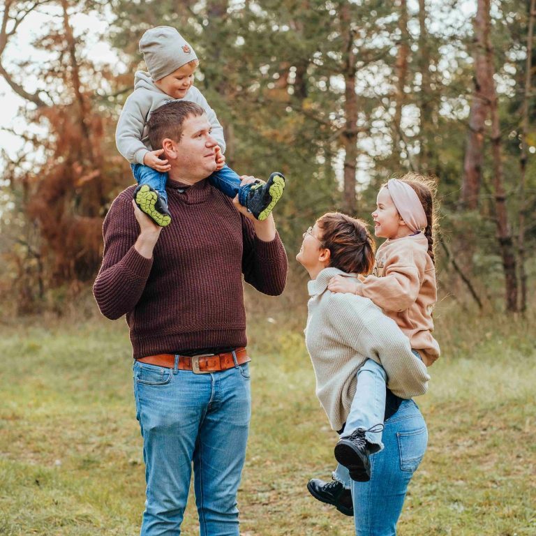 Familie mit zwei Kindern, die draußen in der Natur spielen und Spaß haben.