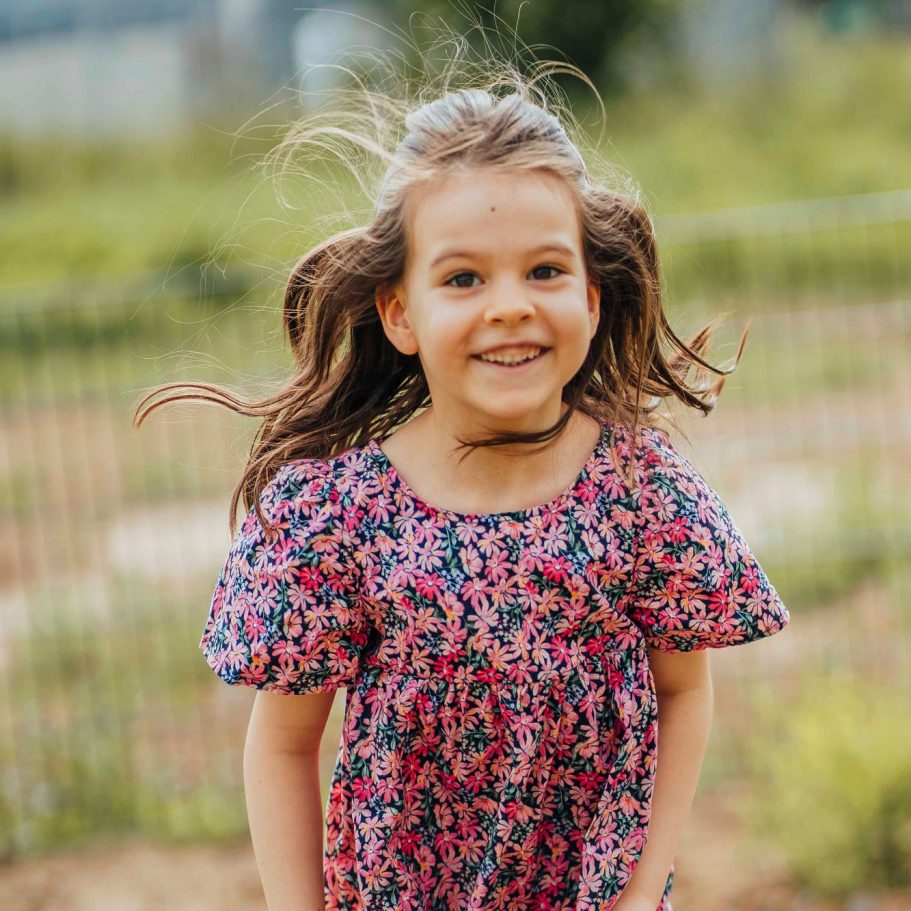 kindergarten bilder wuerzburg Ein fröhliches Mädchen in einem bunten, blumigen Kleid steht lächelnd im Freien.