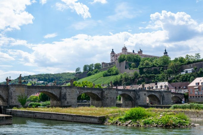 Blick auf eine Brücke im Vordergrund und eine Burg auf einem Hügel im Hintergrund.