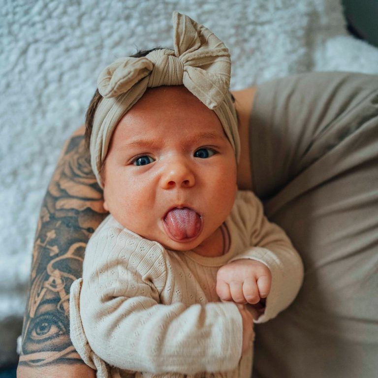 Baby mit einem Haarband macht eine lustige Grimasse und streckt die Zunge heraus.