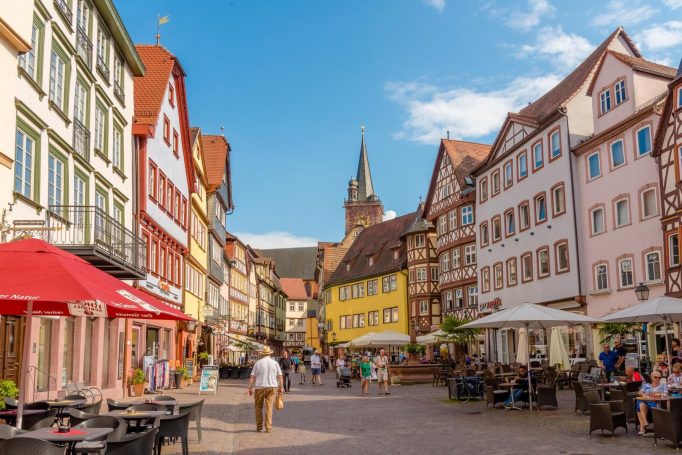 Fotografin Wertheim Bunte Fachwerkhäuser und Cafés in einer lebhaften Stadtstraße mit Menschen.