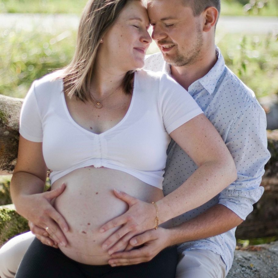 Ein Paar sitzt zusammen, lächelt sich an und hält liebevoll den Babybauch der Frau.