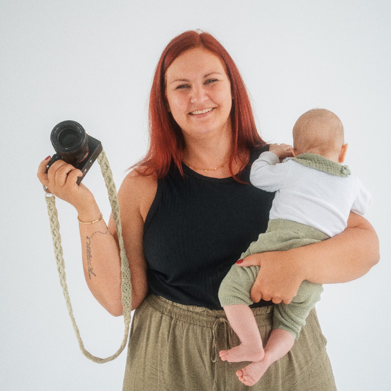 Junge Frau mit rotem Haar trägt Baby in der Trage auf einem Waldweg.