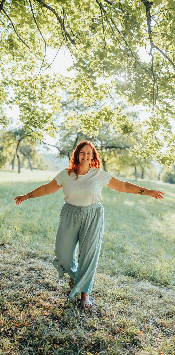 fotograf wertheim Eine Frau mit roten Haaren läuft fröhlich über eine grüne Wiese unter Bäumen.
